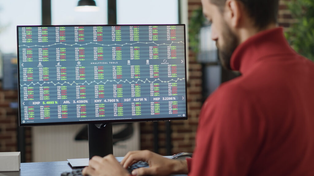 Jovem investidor trabalhando em computador com gráficos de ações em tempo real.